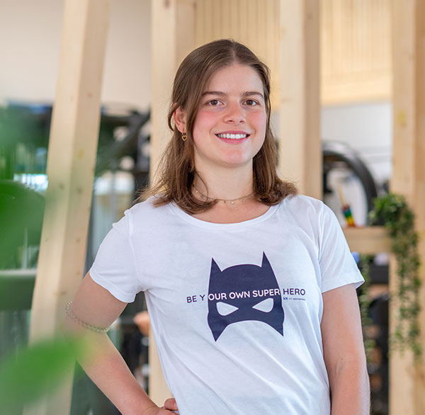 Frau mit T-Shirt ‚Be your own superhero‘ lächelt in einem modernen Innenraum