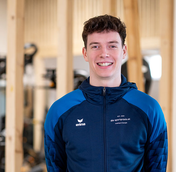 Bernhard in Sportjacke lächelt in die Kamera, im Hintergrund Holzstruktur und Trainingsgeräte