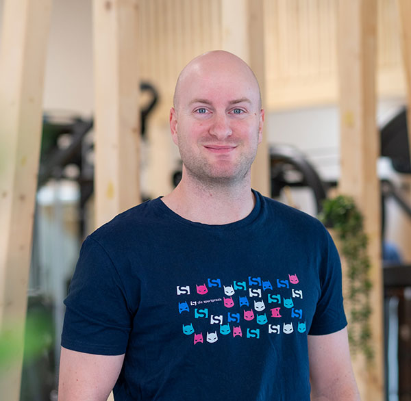 Chrsitan im T-Shirt mit Superheldenmotiv lächelt in modernem Trainingsraum in die Kamera