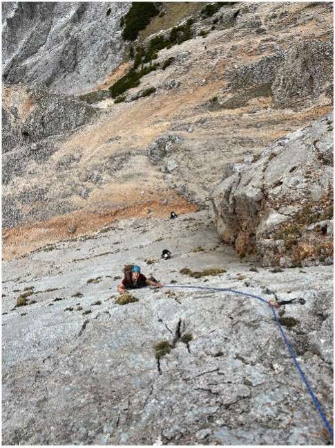 Kletterin mit Seil in steiler Felswand, weitere Kletterer folgen im Hintergrund
