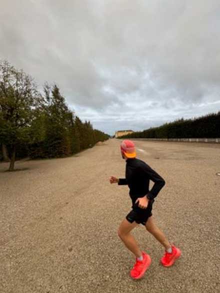 Läufer mit roter Kappe joggt auf breiter Allee unter wolkigem Himmel.