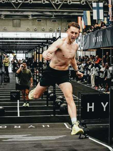 Athlet springt jubelnd ins Ziel einer Fitness-Competition in der Halle.